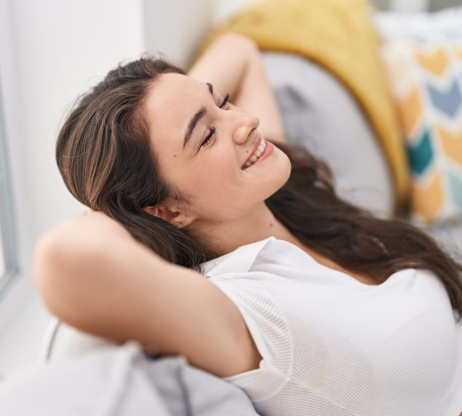 Chica joven sonriente con los brazos en la cabeza medio tumbada